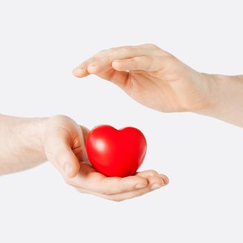 health, medicine and charity concept - close up of male hands with small red heart