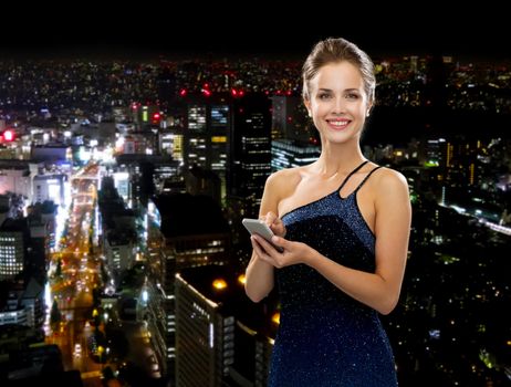 technology, communication and people concept - smiling woman in evening dress holding smartphone over night city background