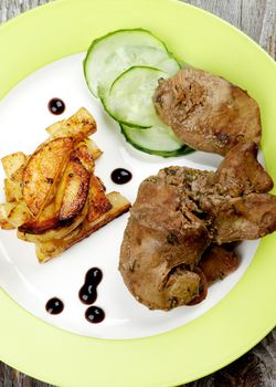 Delicious Roasted Chicken Liver Arranged with Grilled Potato Sticks, Cucumber and Balsamic Sauce on Green Plate on Rustic Wooden background. Top View