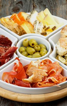 Serving Plate with Spanish Cheeses, Jamon, Cured Ham, Green Olives and Bread Sticks closeup on Rustic Wooden background