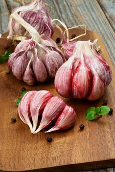 Fresh Raw Pink Garlic Full Body with Greens and Black Peppercorn closeup on Cutting Board on Rustic Wooden background