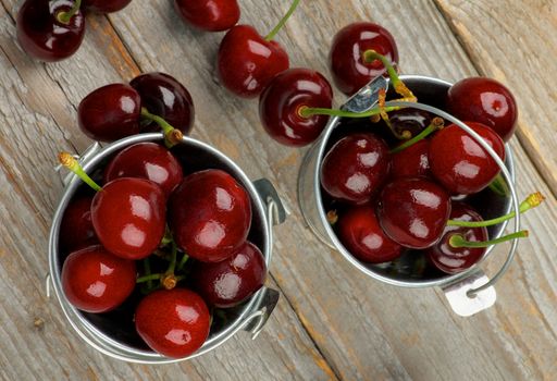 Tin Buckets Full of Sweet Dark Red Cherries closeup on Rustic Wooden background. Top View