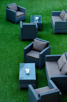 Contemporary Lounge Zone with Wicker Chairs with Comfortable Pillows and Tables on Perfect Green Grass Outdoors 