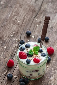 Serving of Yogurt with Whole Fresh Blueberries, Raspberries and Oatmeal on Old Rustic Wooden Table with Copyspace