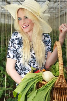 Close up Happy Blond Woman Wearing Fashionable Off-White Straw Hat, Carrying Basket of Fresh Vegetables in the Farm and Looking Into the Distance.