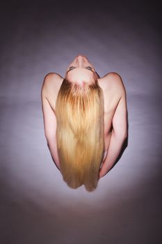 High Angle View of a Bare Young Woman with Long Blond Hair, Sitting on an Empty Floor and Facing with Eyes Closed.