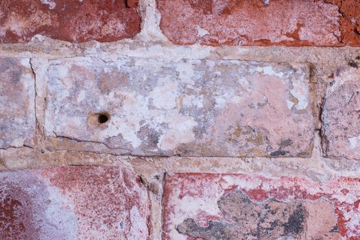 aged interior brick wall with worn and damaged brickwork and drill hole