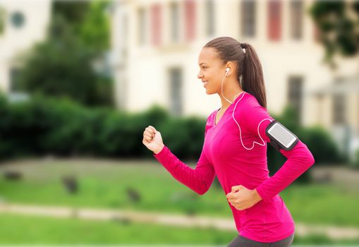 sport, fitness, health, technology and people concept - smiling young african american woman running with smartphone and earphones outdoors