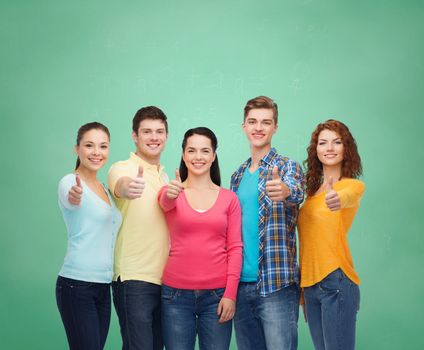 friendship, education, school and people concept - group of smiling teenagers showing thumbs up over green board background