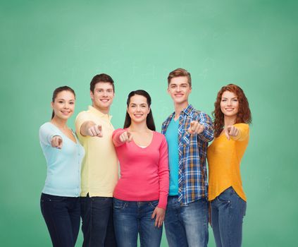 friendship, education, school and people concept - group of smiling teenagers pointing finger on you over green board background