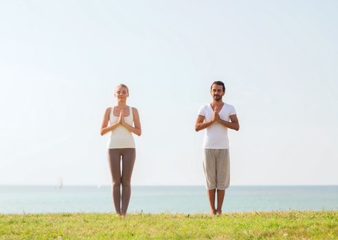 fitness, sport, friendship and lifestyle concept - smiling couple making yoga exercises outdoors