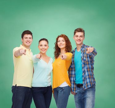 friendship, education, school and people concept - group of smiling teenagers pointing finger on you over green board background