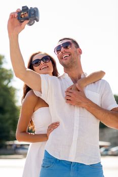 love, wedding, summer, dating and people concept - smiling couple wearing sunglasses making selfie with digital camera in park