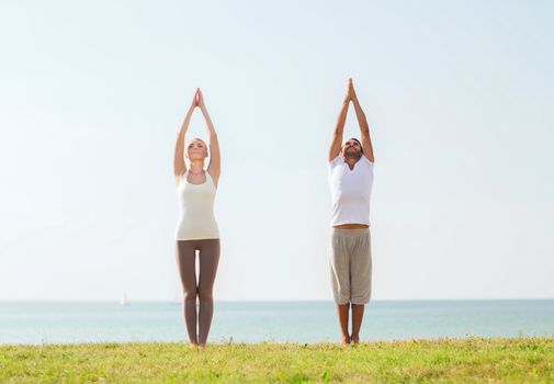 fitness, sport, friendship and lifestyle concept - smiling couple making yoga exercises outdoors