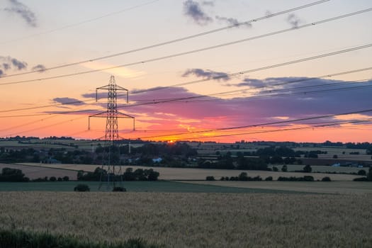 sunset shot of electricity pylon in field with multiple power lines