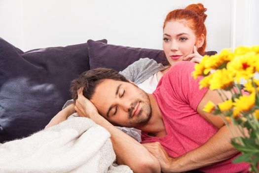 Young Couple Relaxing on the Couch In the Living Room, with Pensive Facial Expressions, While Boyfriend is Lying on the Lap of her Girlfriend.