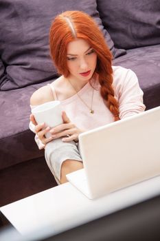 Pretty Young Woman Using her Laptop Computer In the Living Room with Feet on the Table and Showing Serious Face.