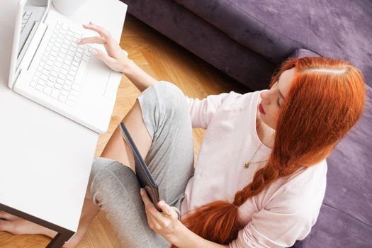 Pretty Young Woman Using her Laptop Computer In the Living Room with Feet on the Table and Showing Serious Face.