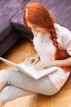 Pretty Young Woman Using her Laptop Computer In the Living Room with Feet on the Table and Showing Serious Face.