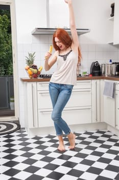 Happy Pretty Young Woman Holding a Banana Fruit, Dancing Alone at the Kitchen Inside the Home.