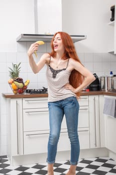 Happy Pretty Young Woman Holding a Banana Fruit, Dancing Alone at the Kitchen Inside the Home.