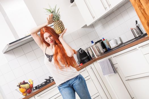 Happy Young Woman Using a Pineapple Fruit as Microphone While Singing Out Loud In the Kitchen.