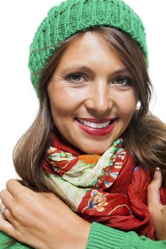 Cute sexy young woman with long brunette hair in a green winter outfit smiling playfully at the camera with her hand to her red scarf, on white