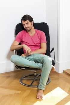 Young Man in Casual Clothing Sitting on Black Chair While Reading a Book and Holding a Glass of Drink.