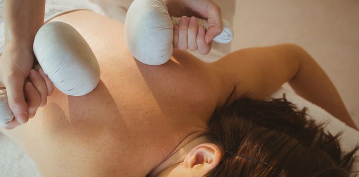 Young woman getting herbal compress massage in therapy room