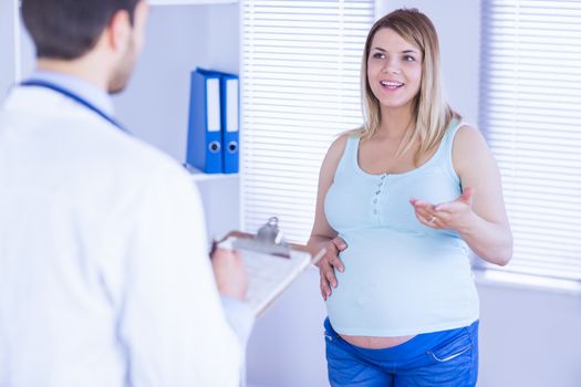 Smiling pregnant patient talking to doctor which is taking notes in medical office