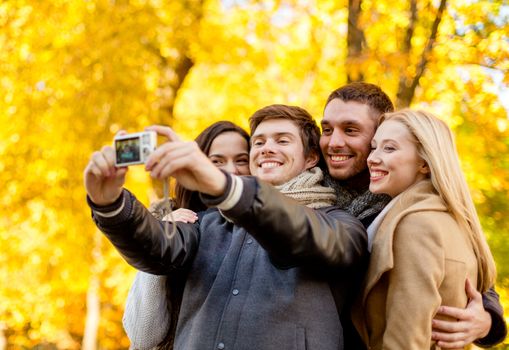 relationship, season, friendship, technology and people concept - group of smiling men and women making self portrait with digital camera in autumn park