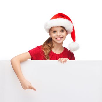 christmas, xmas, holidays and advertisement concept - happy girl child in santa helper hat pointing finger on blank white board