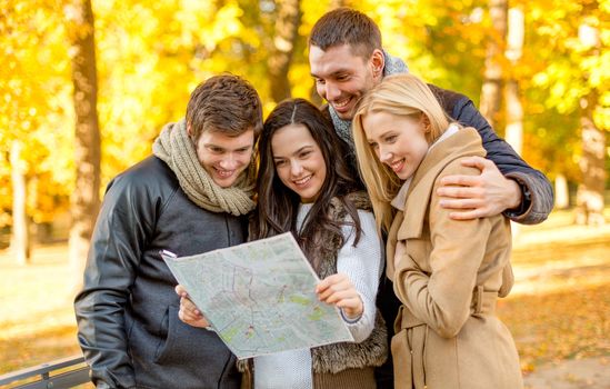 travel, vacation, people, tourism and friendship concept - group of smiling friends looking to map in city park