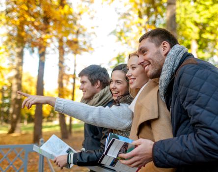 travel, people, tourism, gesture and friendship concept - group of smiling friends with map standing on bridge and pointing finger in city park