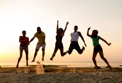 friendship, summer vacation, holidays, party and people concept - group of smiling friends dancing and jumping on beach