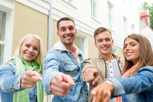 travel, vacation and friendship concept - group of smiling friends in city pointing finger at you