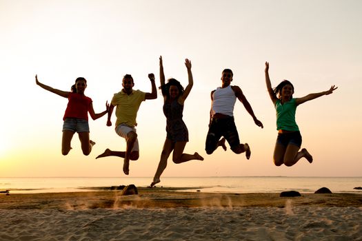 friendship, summer vacation, holidays, party and people concept - group of smiling friends dancing and jumping on beach