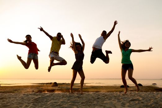 friendship, summer vacation, holidays, party and people concept - group of smiling friends dancing and jumping on beach