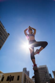 Athletic woman doing yoga on bollard in the city