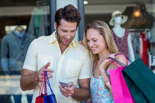 Smiling couple with shopping bags looking at smartphone at shopping mall