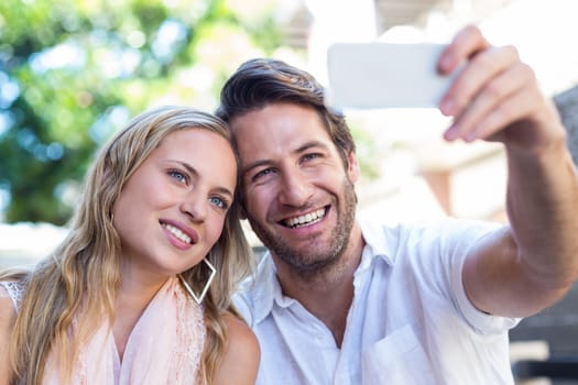 Smiling couple sitting and taking selfies at shopping mall