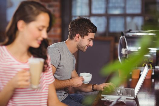 Smiling young man sitting at bar and using laptop at coffee shop