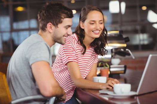 Smiling friends using laptop and having coffee together at coffee shop