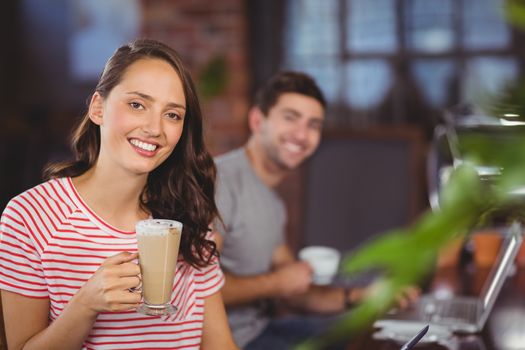 Portrait of smiling young woman with latte in front of her friend at coffee shop