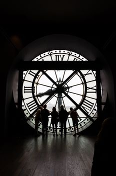 Paris, France - May 14, 2015: Silhouettes of unidentified tourists looking through the clock with roman numerals in the museum D'Orsay. The museum houses the largest collection of impressionist and post-impressionist masterpieces in the world.