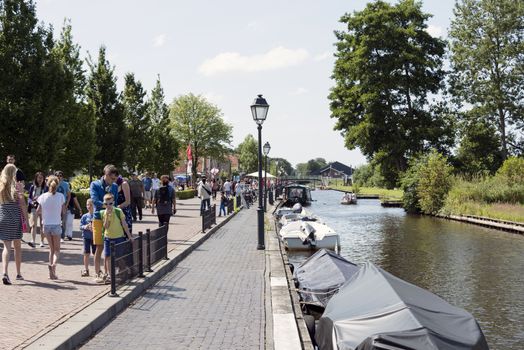 GIETHOORN, NETHERLANDS - JULY 18, 2015: Unknown tourists walking near the canals with the boats  in Giethoorn on july 18 2015. The beautiful houses and gardening city is know as "Venice of the North"