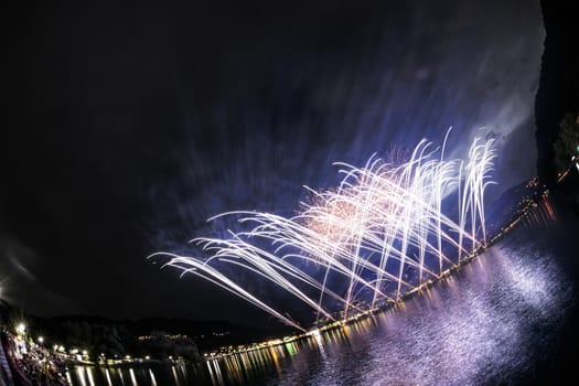 Fireworks on the Lugano Lake in a summer evening seen from lakefornt of Lavena-Ponte Tresa, Lombardy - Italy