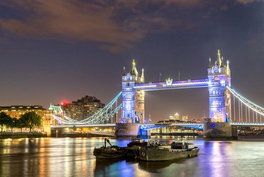The Tower Bridge at night with boats on Thames river - London - UK.