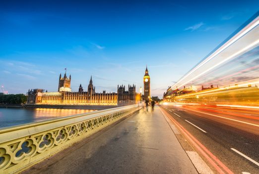 Bus light trails across Wetminster Bridge with blurred moving people towards Big Ben.