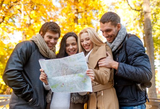 travel, vacation, people, tourism and friendship concept - group of smiling friends looking to map in city park